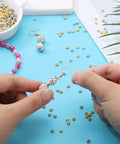 2000 Pcs Gold And Silver Spacer Beads 4Mm Flat Round Disc Beads For DIY Jewelry Making Bracelets And Necklaces Gold Tone And Silver Tone 1.5Mm Hole 4x1.7Mm Bulk Craft Supplies For Bead Crafters with hands assembling jewelry on blue background.