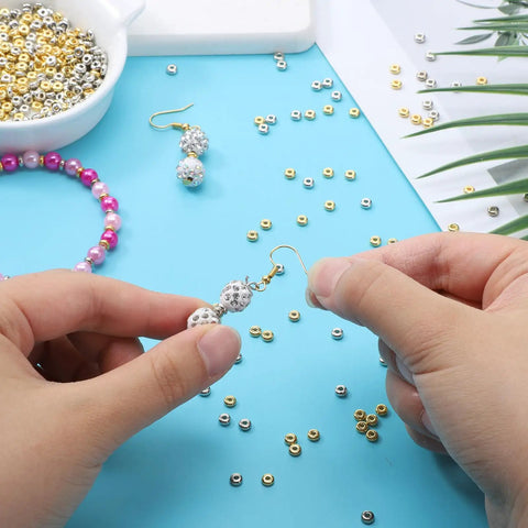 2000 Pcs Gold And Silver Spacer Beads 4Mm Flat Round Disc Beads For DIY Jewelry Making Bracelets And Necklaces Gold Tone And Silver Tone 1.5Mm Hole 4x1.7Mm Bulk Craft Supplies For Bead Crafters with hands assembling jewelry on blue background.