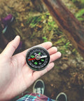 Hand holding Miniature Bubble Compass For Outdoor Hiking And Camping Navigation Tool Durable Acrylic Easy Read Dial