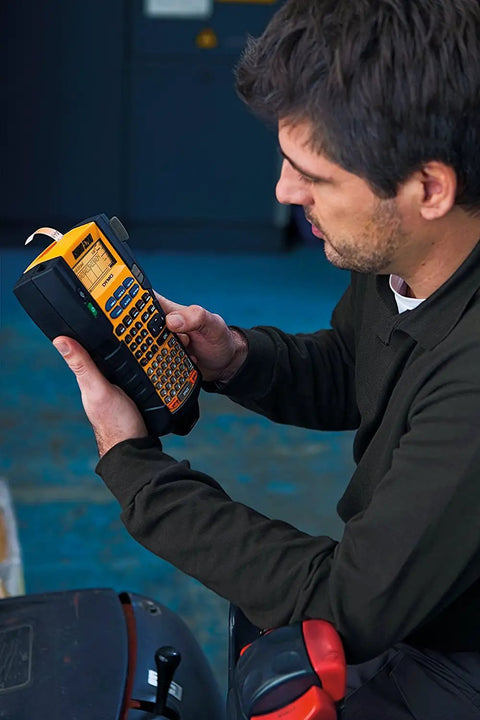 Person using Rhino 5200 Label Maker With One Touch Hot Keys For Speedy, Durable Asset Labeling On Job Sites in industrial setting.