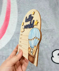 Hand holding Hot Air Balloon Arch Birth Announcement Sign with 3D Hello World Text and safari animal passengers in nursery