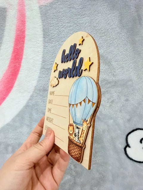 Hand holding Hot Air Balloon Arch Birth Announcement Sign with 3D Hello World Text and safari animal passengers in nursery