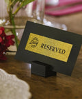 Black reserved sign with gold label on a wooden table, labeled using P-Touch CUBE Plus Bluetooth Label Maker PT-P710BT.