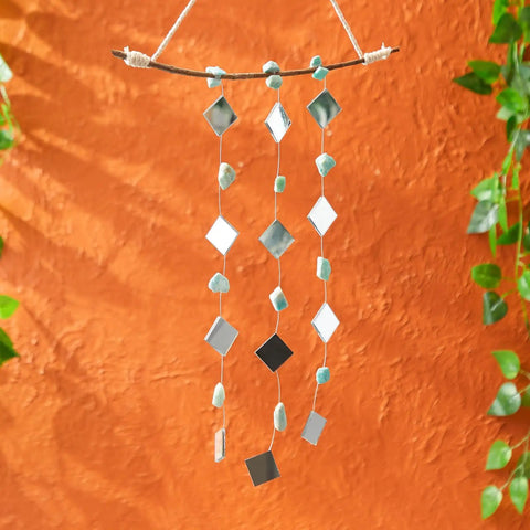 120 Pack Mini Square Mirror Tiles 1x1 Inch For Mosaic Art And Crafts hanging on strings for DIY home decor against an orange wall.