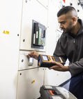 A technician using a Heavy Duty Industrial Label Printer Hooks Up Smooth Via Bluetooth Features Dual Auto Cutters for tape on a panel.