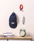 Movelyst clear adhesive wall hooks with strips; front view holds navy cap, red earphones, and glasses.