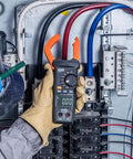 Electrician using Auto Ranging Digital Clamp Meter With True RMS For AC And DC Current And Voltage Resistance in panel box.