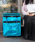 Person sitting next to Glitter Blue Rolling Grocery Tote With Wheels And Zipper Covered 8 Pocket Organizer Foldable Durable Tote