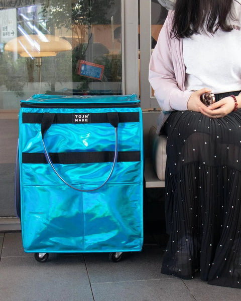 Person sitting next to Glitter Blue Rolling Grocery Tote With Wheels And Zipper Covered 8 Pocket Organizer Foldable Durable Tote