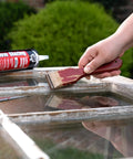 Person applying Latex Window Glazing Sealant White 10.1 Oz for wood and metal window frames with putty knife