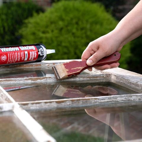 Person applying Latex Window Glazing Sealant White 10.1 Oz for wood and metal window frames with putty knife