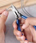 Hands using precision flush cutters and wire cutters for electronics and DIY projects on a wire, close-up view of the pliers.