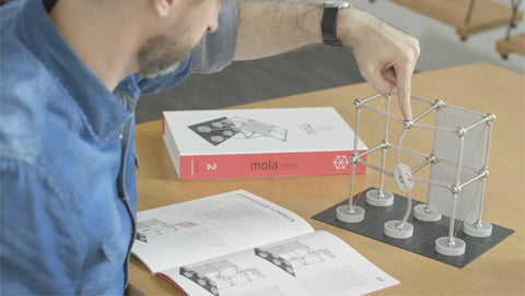 Person using Structural Kit 2 Magnetic Modular System for engineering education with 145 pieces on table.