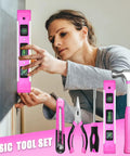 Woman using Pink Tool Set For Women 130 Piece Home Toolkit including level, pliers, screwdriver, and hammer.
