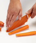 Orange plastic crinkle-cut knife for vegetables with a wavy blade used to slice carrot sticks.