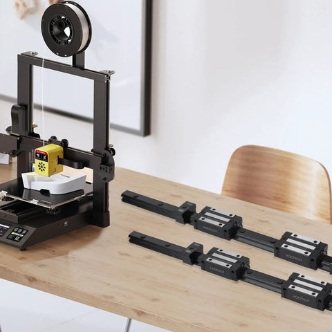 3D printer next to two 450mm linear guide rails kit with four carriage blocks and four end stops on a wooden table