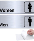 Two Pack Aluminum Restroom Signs For Men And Women Self Adhesive Metal Bathroom Door Wall Signage For Offices Restaurants Public Places 9 By 3 Inches Silvery Finish Easy Mount showing "Women" and "Men" signs.