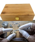 Watch repair scene with hands using Pro Grade 20 Calibers Watch Mainspring Winder Kit With Barrels And Copper Tools next to wooden box.