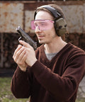 Person wearing Anti Fog Safety Goggles For Men And Women With Blue Light Blocking UV Protection Dust Resistant Coating Scratch Resistant Lenses Pink Frame Unisex Eyewear For Work Home Or Travel Clear Vision And All Day Comfort, using a firearm outdoors, wearing earmuffs.