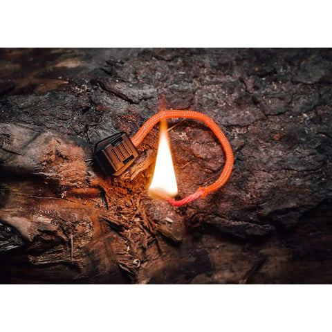 TinderZIP Zipper Pull Fire Starter With Built In Tinder igniting on a log, showcasing its ability for quick sparks in outdoor conditions.