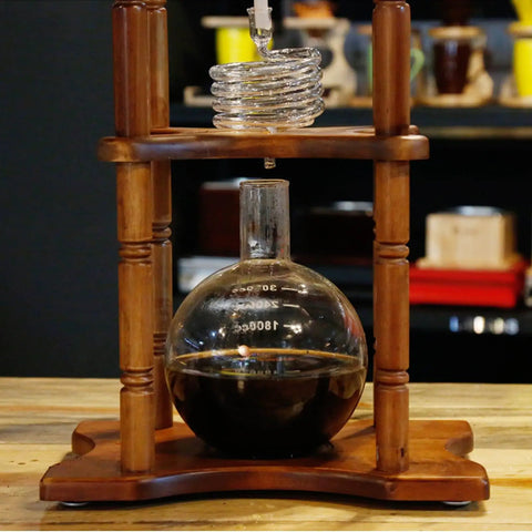 Slick Cold Brew Coffee Tower Featuring A Reliable Ice Drip System For Bold Flavor Kick Holds A Humongous 3000ML Glass Jar Settled On A Raw Brown Wood Stand.