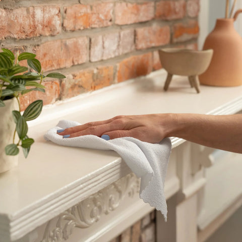 Microfiber cleaning cloth, white, being used to wipe a white mantel against a brick wall.