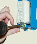 Person using a drill on a blue electrical outlet box with white receptacle, demonstrating Knockout 120 Piece Electrician Screw Kit Featuring 8-32 Round Phillips Head Machine Screws In Six Assorted Lengths A Total Job Site Staple For Switches Receptacles And Outlet Wiring.
