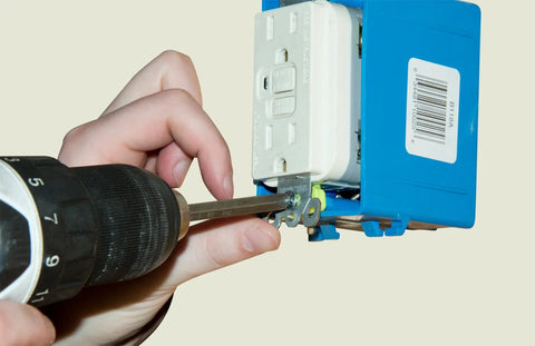 Person using a drill on a blue electrical outlet box with white receptacle, demonstrating Knockout 120 Piece Electrician Screw Kit Featuring 8-32 Round Phillips Head Machine Screws In Six Assorted Lengths A Total Job Site Staple For Switches Receptacles And Outlet Wiring.