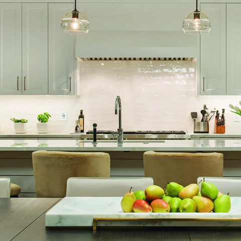 Modern kitchen with pendant lights, white cabinets, and a bowl of fruit on the counter.