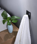 Matte black Adhesive Hooks 4 Pack Towel And Coat Hooks For Wall Mounting Stick On Bathroom Kitchen next to a towel and plant