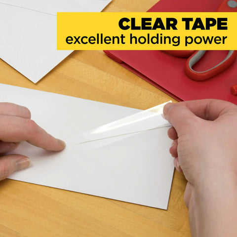 Clear Portable Tape For Office And Home, Versatile Transparent Adhesive On Four Dispensing Rolls, Three Quarter Inch By Eight Hundred Fifty Inches Each, Glossy Finish That Sticks Instantly On Glass, Plastic, And Paper being used to seal an envelope on a wooden desk with scissors in the background.