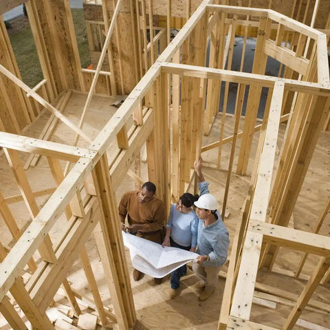 Construction workers discussing plans for framing with wooden beams in a building under construction.