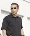 Mens Short Sleeve Uniform Polo Shirt In Black Built For The Daily Grind With Hella Fast Moisture Wicking To Keep You Chill And Fade Proof Pique Polyester That Holds Its Shape Plus A Smart Casual Cut Done Right For Any Working Crew Out Here, worn by a security officer in a professional setting.