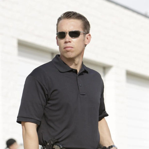 Mens Short Sleeve Uniform Polo Shirt In Black Built For The Daily Grind With Hella Fast Moisture Wicking To Keep You Chill And Fade Proof Pique Polyester That Holds Its Shape Plus A Smart Casual Cut Done Right For Any Working Crew Out Here, worn by a security officer in a professional setting.