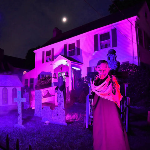 House illuminated by Purple Solar LED Spotlight 2 Pack Outdoor Waterproof Landscape Lights with Halloween decor at night