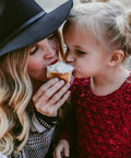 Woman and child sharing a dessert together outdoors, both wearing cozy clothing.