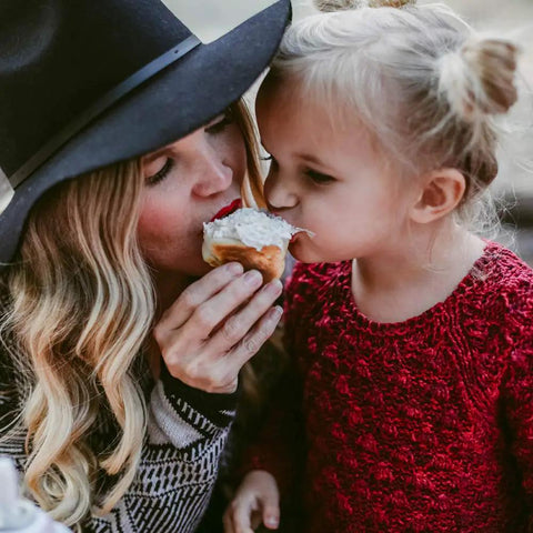 Woman and child sharing a dessert together outdoors, both wearing cozy clothing.
