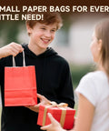 Teen holding red paper bag from Kraft Gift Bags With Handles Bulk Pack 24 Small Party Favor Bags In 6 Colors, 5.8 By 3.2 By 8.25 Inches