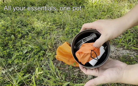 Hands holding Titanium 1100ml Pot And Pan Set For Backpacking with contents inside, mesh bag on grass, outdoor setting