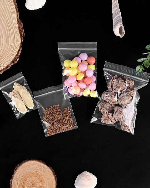 500 Pack Small Clear Resealable Plastic Bags With Four Size Options For Jewelry Candy Pills And More, Durable Reusable Poly Bags For Packaging Storage And Organization Grab And Go Ready with candies and dried fruits inside on black background.