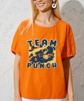 Woman wearing orange t-shirt with Team Punch graphic print, standing against a textured wall background.