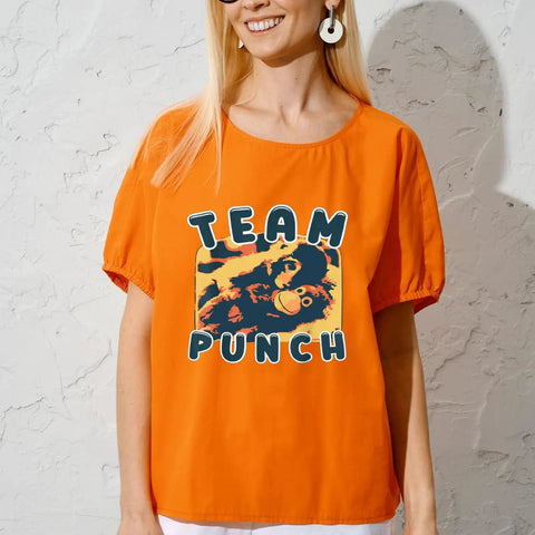 Woman wearing orange t-shirt with Team Punch graphic print, standing against a textured wall background.