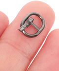 Close-up of a tiny black alloy buckle on a fingertip, part of Dope 150Pcs Mini Buckle Set Alloy Tiny Buckles For DIY Doll Clothes Sewing Crafts