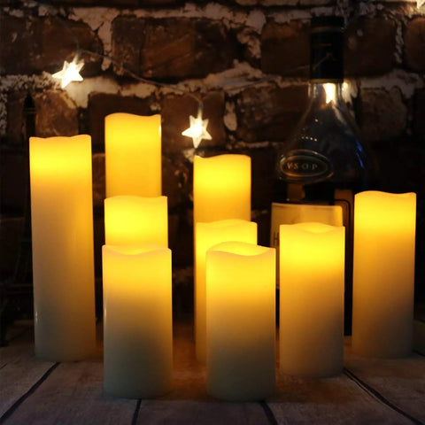 Nine Piece Flameless LED Wax Pillar Candles Set With Remote Timers Real Wax Ivory Finish Heights 4 Inch 5 Inch 6 Inch 7 Inch 8 Inch 9 Inch 2.2 Inch Diameter Battery Powered For Home Fireplace Decor Weddings And Festivals glowing on a table