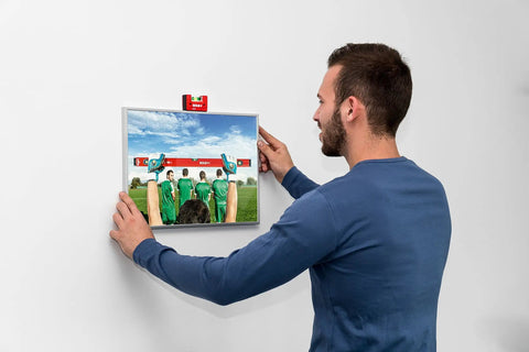 User leveling a picture frame with Sola Spirit Level Compact Go! Clip, 0 mounted on top for accurate alignment.