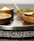 Slick Brushed Stainless Steel Lazy Susan Turntable with wooden bowls holding spices on a braided mat.