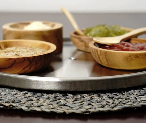Slick Brushed Stainless Steel Lazy Susan Turntable with wooden bowls holding spices on a braided mat.