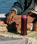 Heavy Duty Double Walled Stainless Steel Water Bottle 24 Oz next to a person enjoying a picnic with apples by the water.