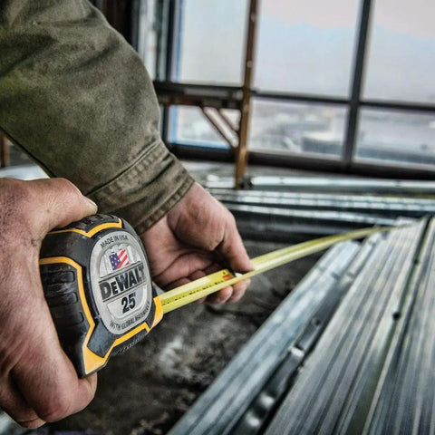Person using 25 ft tape measure with 1-1/4 inch tape for accurate measurements in carpentry project, visible framing structure