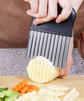 Crinkle cutter with black handle and stainless steel blades slicing a potato.